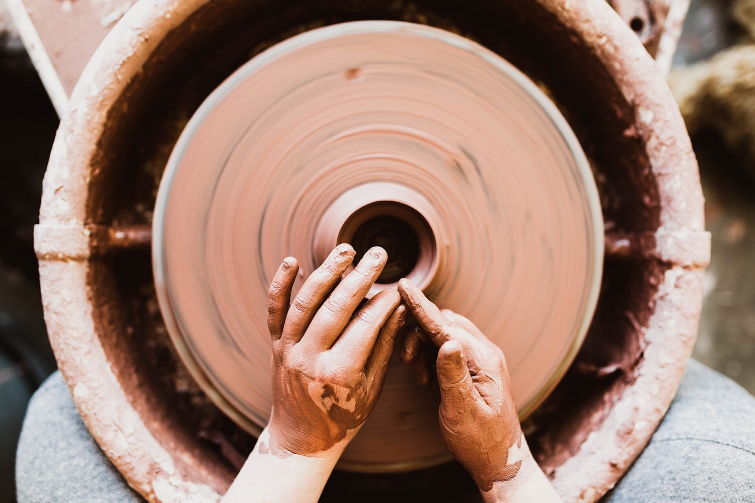Hands shaping wet clay on a potter's wheel